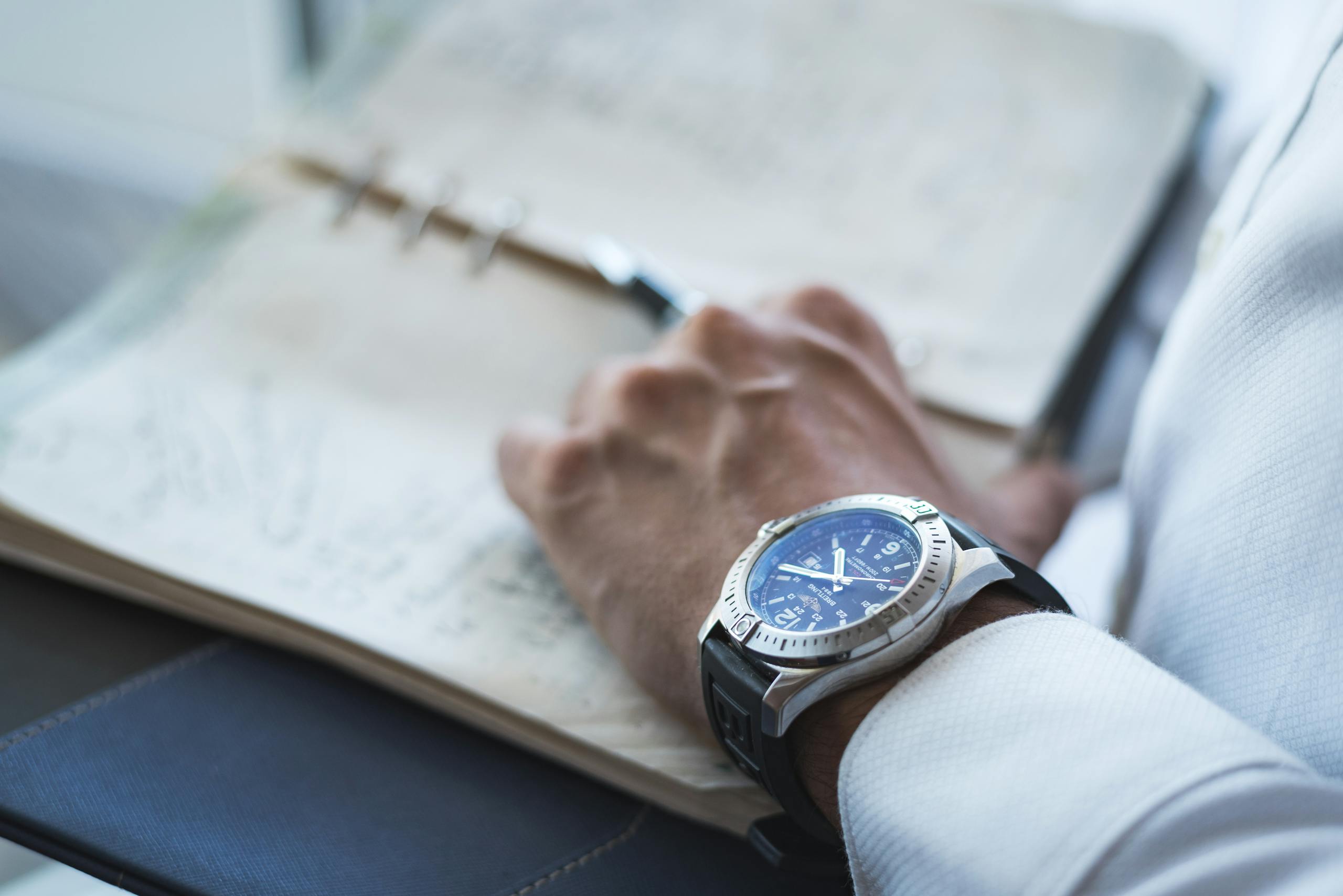 Detailed shot of a wristwatch and an open leather-bound notebook, showing a handwritten page.